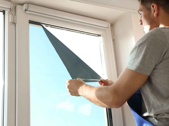 Professional worker tinting window with foil indoors